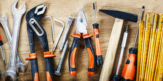 Werkzeuge - Hammer, Zangen, Zollstock, Säge - liegen aufgefächert auf Holz.