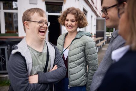 Eine Gruppe - Menschen mit und ohne Behinderung - steht lachend zusammen.