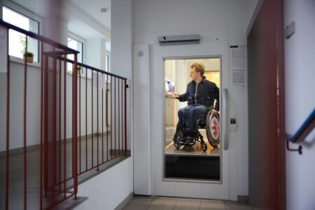 Junger Mann im Rollstuhl bedient Aufzug im Wohnhaus.