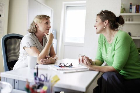Zwei Frauen sitzen an einem Tisch und unterhalten sich.