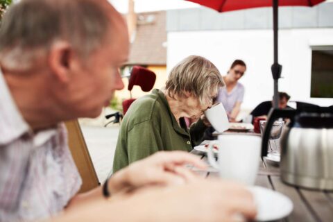 Mehrere Menschen trinken Kaffee am Tisch, auf einer Terrasse.