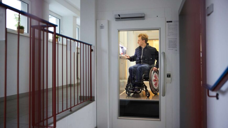 Junger Mann im Rollstuhl bedient Aufzug im Wohnhaus.