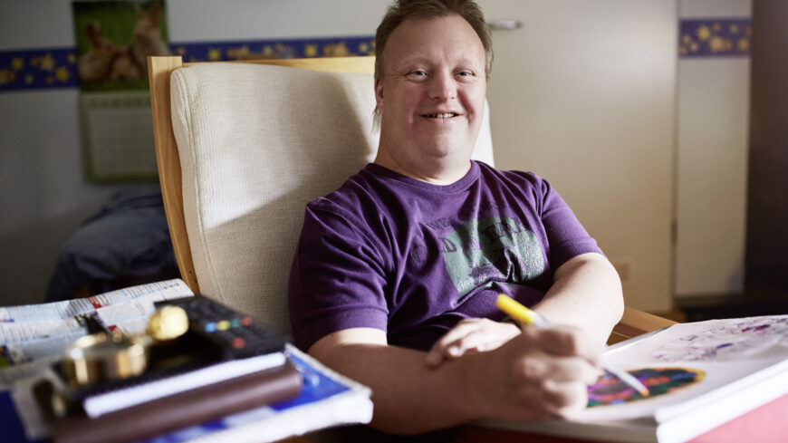 Junger Mann malt in seinem Zimmer zufrieden ein Mandala.