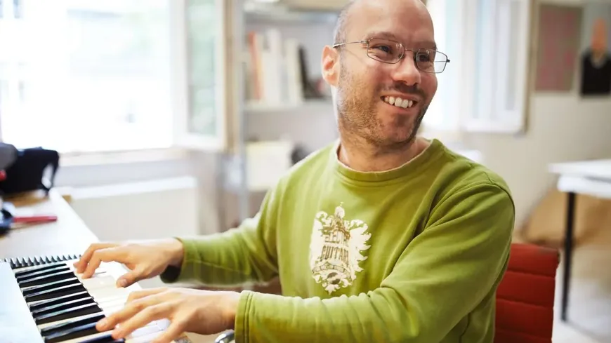 Ein junger Mann mit Brille spielt Klavier und lächelt.